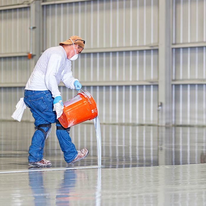 A construction worker pours epoxy paint onto a warehouse floor